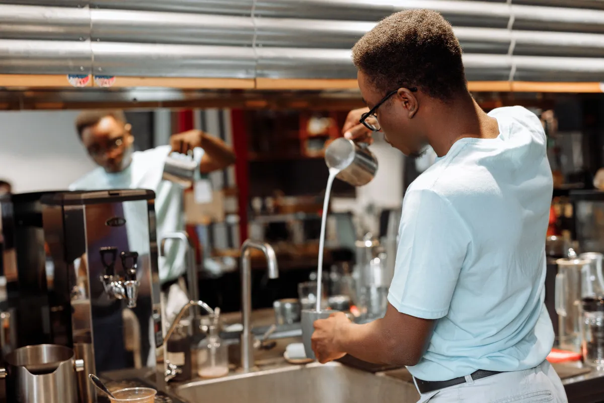 Barista nalévá latte art do šálku na baru